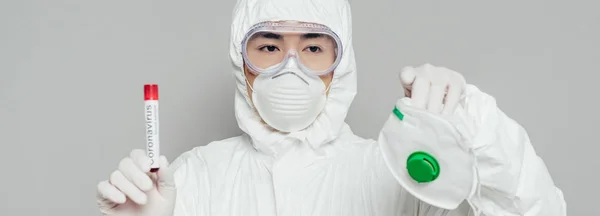 Prise de vue panoramique de l'épidémiologiste asiatique montrant masque respirateur et éprouvette avec échantillon de sang isolé sur gris — Photo de stock