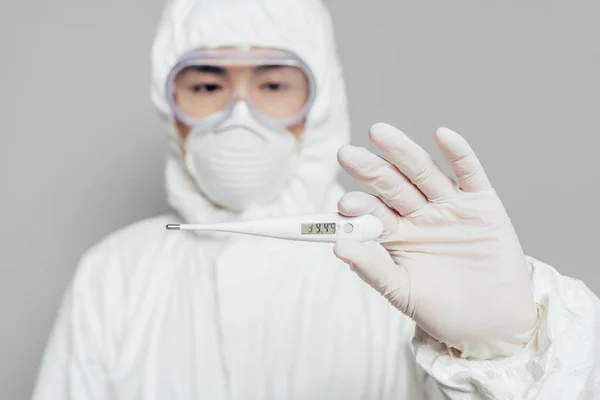 Foco selectivo de epidemiólogo asiático sosteniendo termómetro que muestra alta temperatura aislado en gris, tiro panorámico - foto de stock