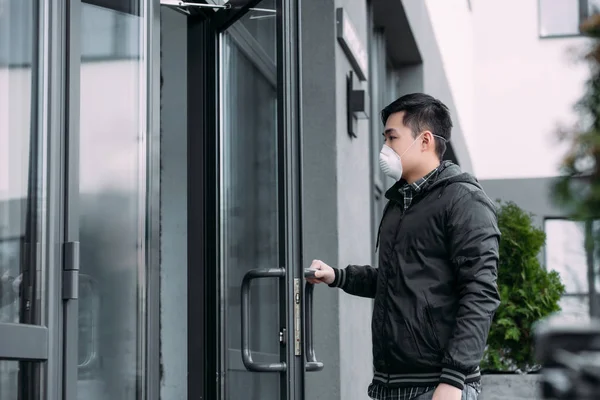 Giovane asiatico uomo in respiratore maschera apertura porta e entrare edificio — Foto stock