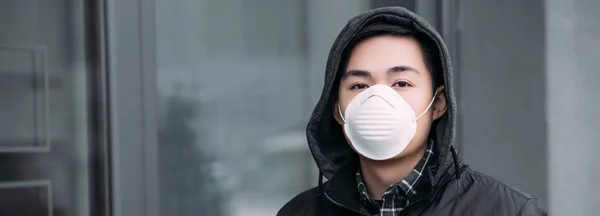 Panoramic shot of young asian man in respirator mask looking at camera while standing on street — Stock Photo