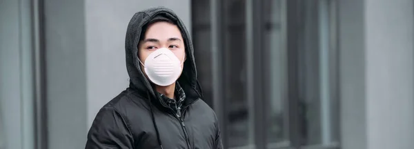 Panoramic shot of young asian man in respirator mask looking away while standing on street — Stock Photo