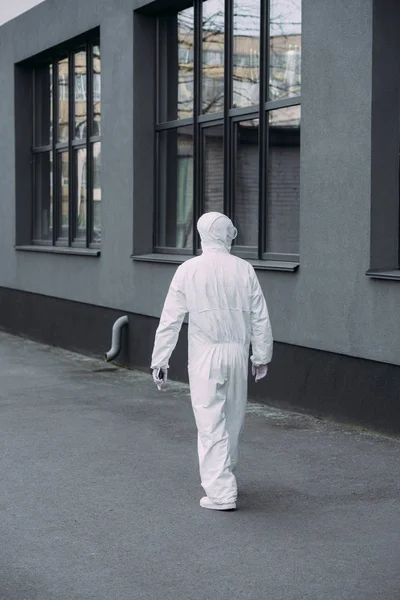 Vue arrière de l'épidémiologiste en combinaison de danger marchant le long du bâtiment — Photo de stock