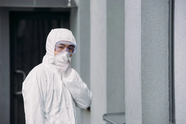 Азиатский эпидемиолог в защитном костюме и респираторной маске, смотрящий в камеру, стоя снаружи — стоковое фото