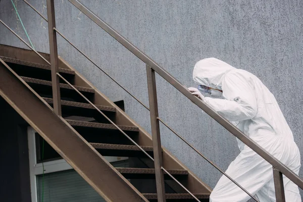Épidémiologiste asiatique en combinaison Hazmat et masque respirateur marchant à l'étage à l'extérieur du bâtiment — Photo de stock