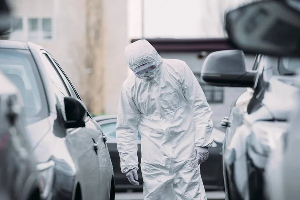 Selektiver Fokus des asiatischen Epidemiologen in Warnanzug und Atemschutzmaske bei der Kontrolle von Fahrzeugen auf Parkplätzen — Stockfoto