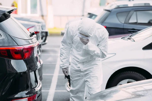 Asiatischer Epidemiologe in Warnanzug und Atemschutzmaske inspiziert Fahrzeuge auf Parkplatz — Stockfoto