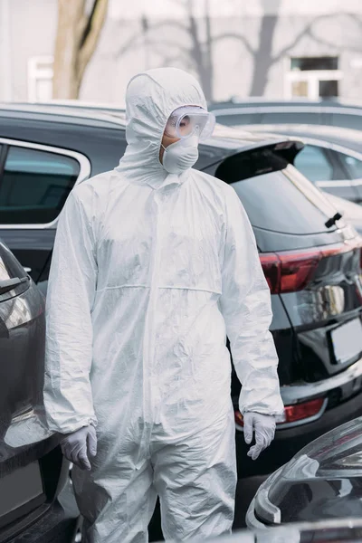 Asian epidemiologist in hazmat suit and respirator mask inspecting cars on parking lot — Stock Photo