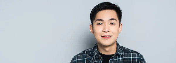 Panoramic shot of young asian man smiling at camera isolated on grey — Stock Photo