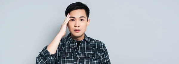 Panoramic shot of young asian man touching forehead and looking at camera isolated on grey — Stock Photo