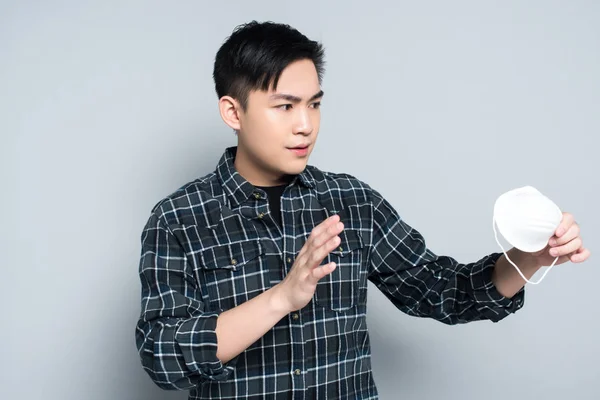 Young asian man showing refuse gesture while holding respirator mask on grey background — Stock Photo