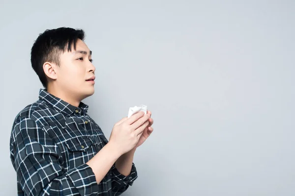 Jovem asiático homem segurando papel guardanapo enquanto sofrendo de corrimento nariz isolado no cinza — Fotografia de Stock