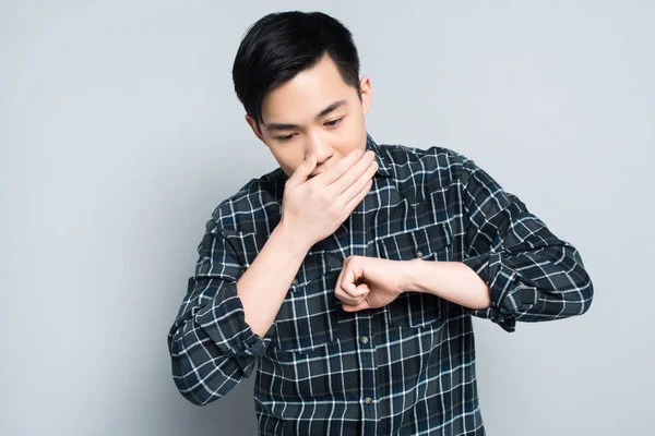 Молодий азіатський чоловік покриває рот при кашлі на сірому фоні — стокове фото