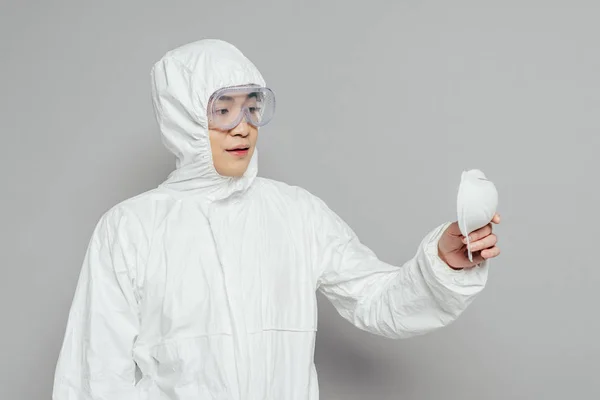 Asiático epidemiólogo en hazmat traje celebración respirador máscara en gris fondo - foto de stock