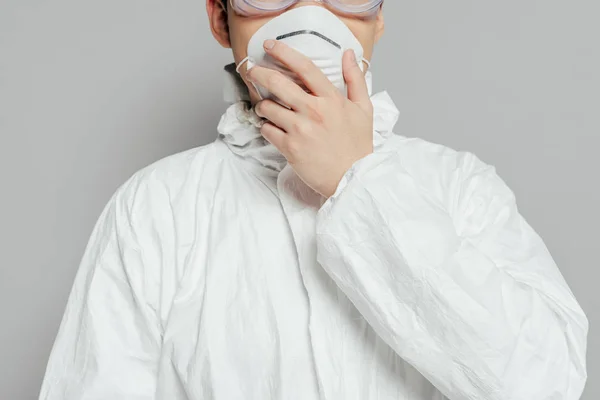 Vue recadrée de l'épidémiologiste en combinaison de danger touchant masque respirateur isolé sur gris — Photo de stock