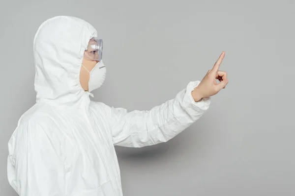 Side view of asian epidemiologist in hazmat suit and respirator mask showing warning gesture on grey background — Stock Photo