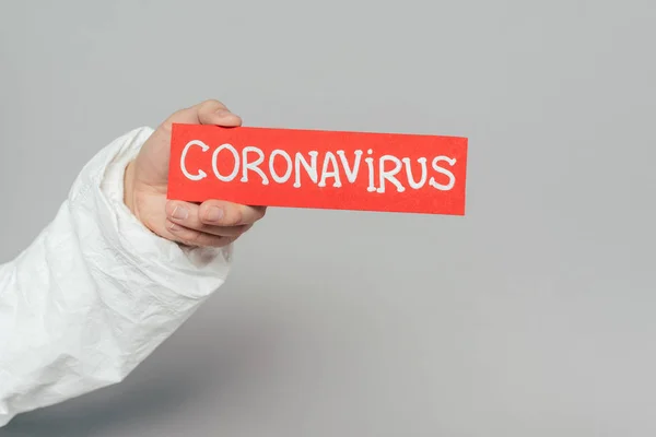 Vista recortada del epidemiólogo con tarjeta de advertencia con inscripción de coronavirus sobre fondo gris - foto de stock