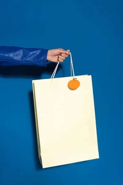 Vista recortada de mujer afroamericana sosteniendo bolsa de compras con etiqueta en blanco en azul - foto de stock