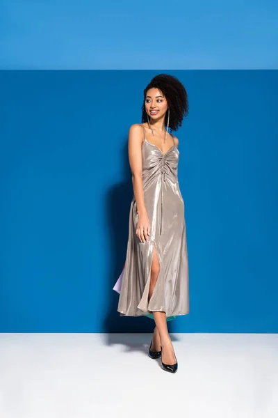 Sonriente hermosa mujer afroamericana en vestido de plata sobre fondo azul - foto de stock