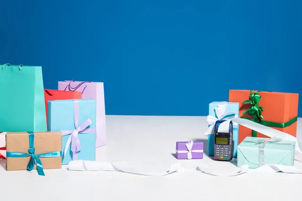 Einkaufstaschen und Geschenkboxen in der Nähe des Zahlungsterminals mit Scheck auf blauem Hintergrund — Stockfoto