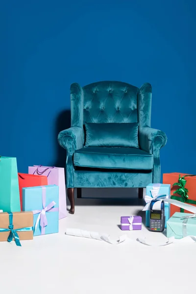 Sacs à provisions et coffrets cadeaux près du terminal de paiement avec chèque sur fond bleu avec fauteuil en velours — Photo de stock