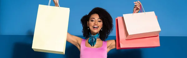 Heureuse femme afro-américaine avec des achats sur fond bleu, vue panoramique — Photo de stock