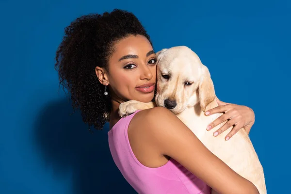 Sorridente afro-americano mulher segurando dourado retriever filhote de cachorro no fundo azul — Fotografia de Stock