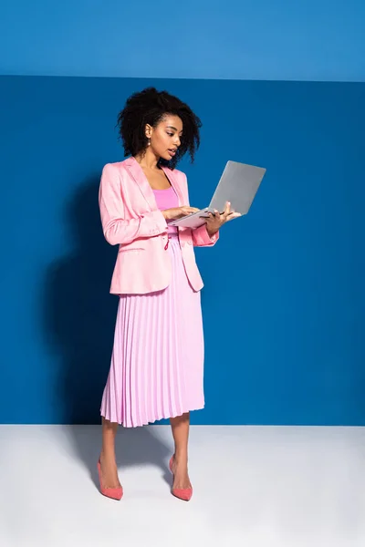 Élégante femme d'affaires afro-américaine utilisant un ordinateur portable sur fond bleu — Photo de stock