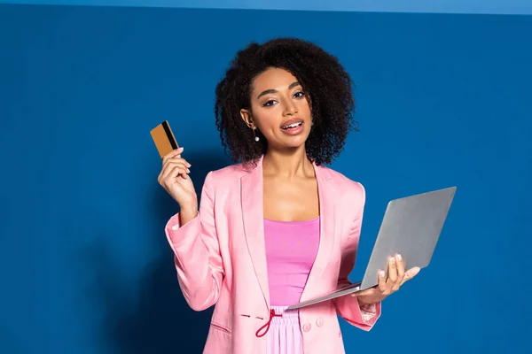 Elegante Africano americano empresária segurando cartão de crédito e laptop no fundo azul — Fotografia de Stock