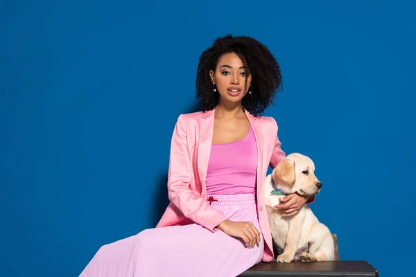 Africano americano mujer sentado con golden retriever cachorro en azul fondo - foto de stock