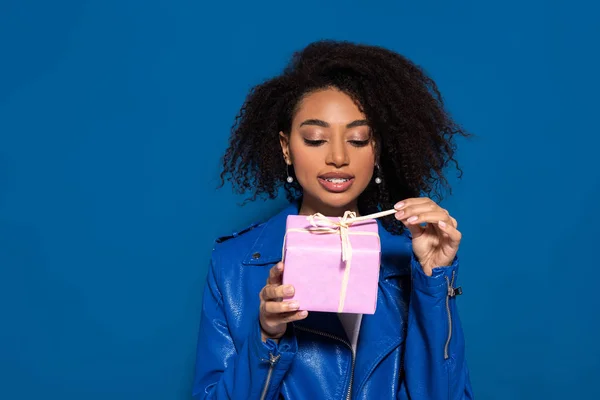 Sonriente mujer afroamericana apertura regalo aislado sobre fondo azul - foto de stock