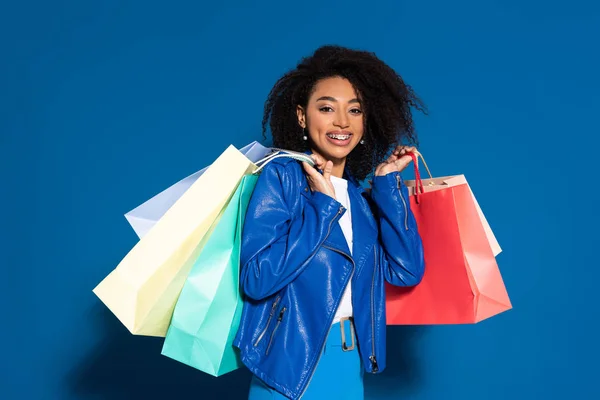 Donna afroamericana sorridente con borse della spesa su sfondo blu — Foto stock