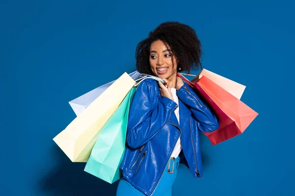 Donna afroamericana sorridente con borse della spesa su sfondo blu — Foto stock