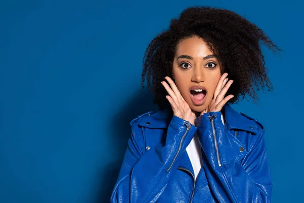 Donna afro-americana scioccata con le mani vicino al viso su sfondo blu — Foto stock