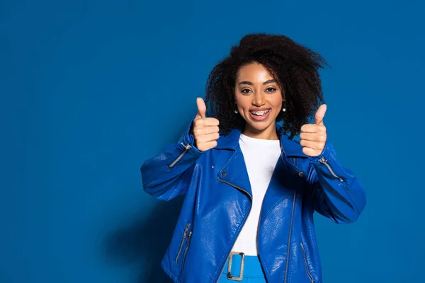 Souriant afro-américaine montrant pouces sur fond bleu — Photo de stock