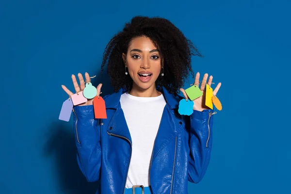 African american woman with open mouth and empty labels on hands on blue background — Stock Photo