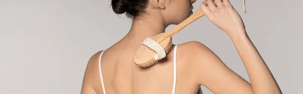 Panoramic shot of woman using massage brush, isolated on grey — Stock Photo