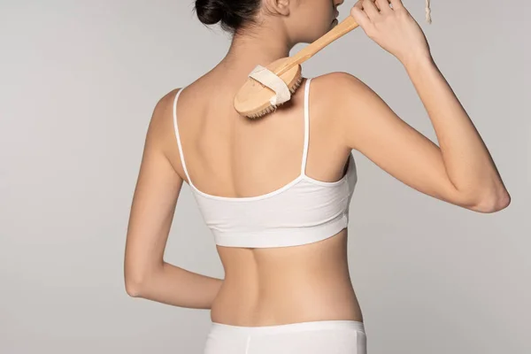 Cropped view of young woman using dry massage brush, isolated on grey — Stock Photo