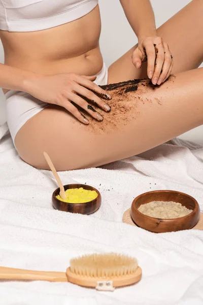 Vue recadrée de fille avec différents gommages et brosse de massage appliquant gommage café sur les jambes — Photo de stock