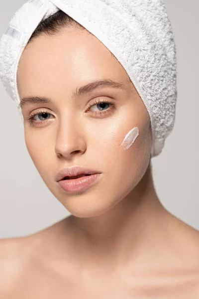 Belle femme avec serviette sur la tête appliquant de la crème cosmétique sur le visage, isolée sur gris — Photo de stock