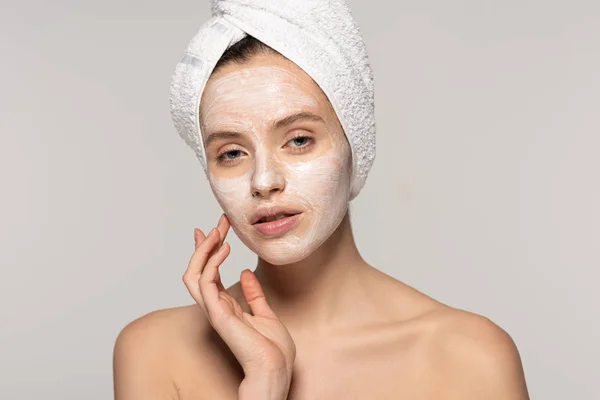 Bella giovane donna con maschera cosmetica sul viso e asciugamano sulla testa, isolata su grigio — Foto stock
