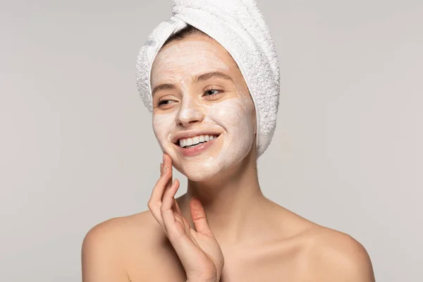 Красивая улыбающаяся девушка с косметической маской на лице и полотенцем на голове, изолированные на сером — стоковое фото