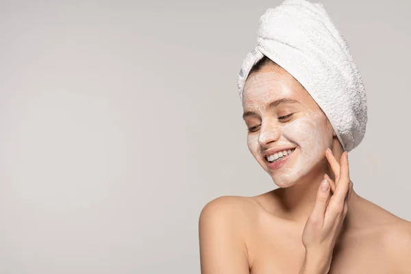 Atractiva chica sonriente con máscara cosmética en la cara y toalla en la cabeza, aislado en gris - foto de stock