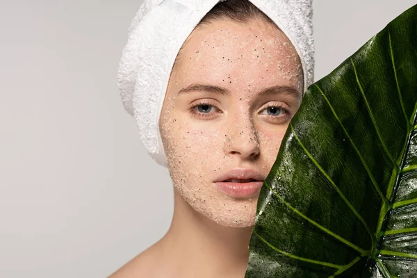 Красивая девушка с полотенцем на голове и кокосовый скраб на лице позируя с листом, изолированные на сером — стоковое фото
