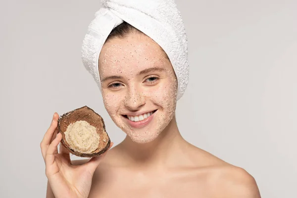 Smiling woman with towel on head holding coconut shell with scrub, isolated on grey — Stock Photo