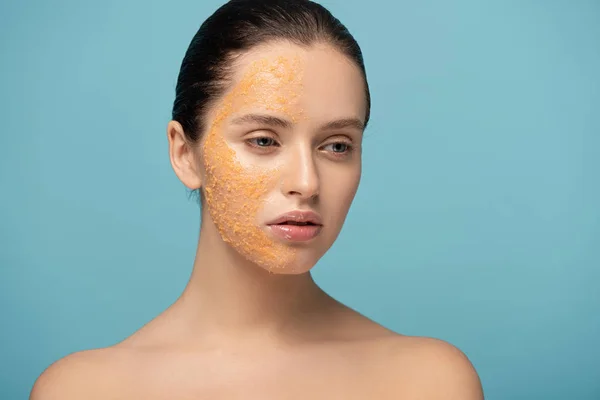 Menina atraente aplicando açúcar amarelo esfoliante no rosto, isolado em azul — Fotografia de Stock