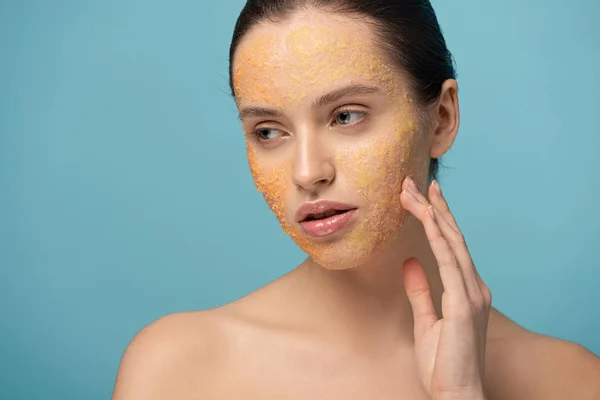 Belle jeune femme appliquant gommage de sucre jaune sur le visage, isolé sur bleu — Photo de stock