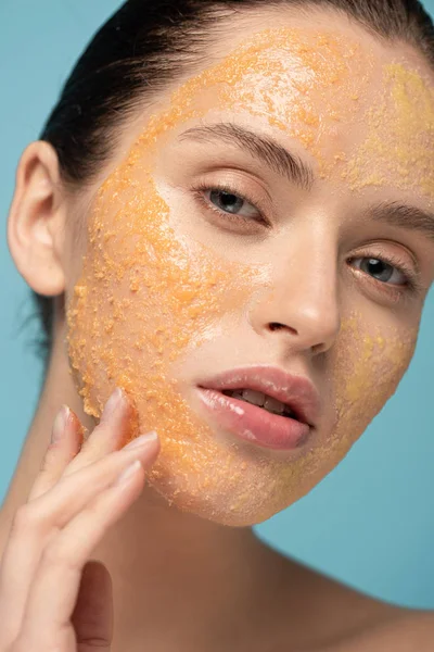 Hermosa chica aplicando amarillo azúcar exfoliante en la cara, aislado en azul - foto de stock