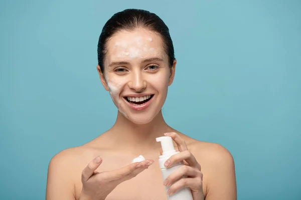 Happy girl applying cleansing foam from bottle, isolated on blue — Stock Photo