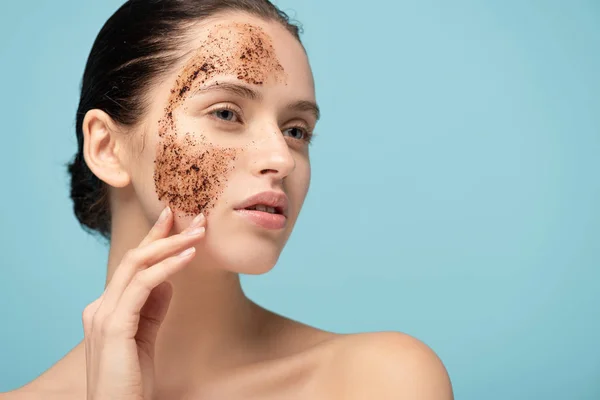 Hermosa mujer aplicando exfoliante de café en la cara, aislado en azul - foto de stock