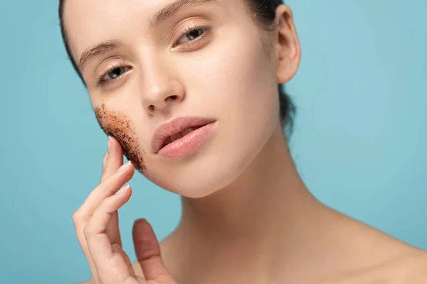 Atractiva mujer que aplica exfoliante de café en la cara, aislado en azul - foto de stock